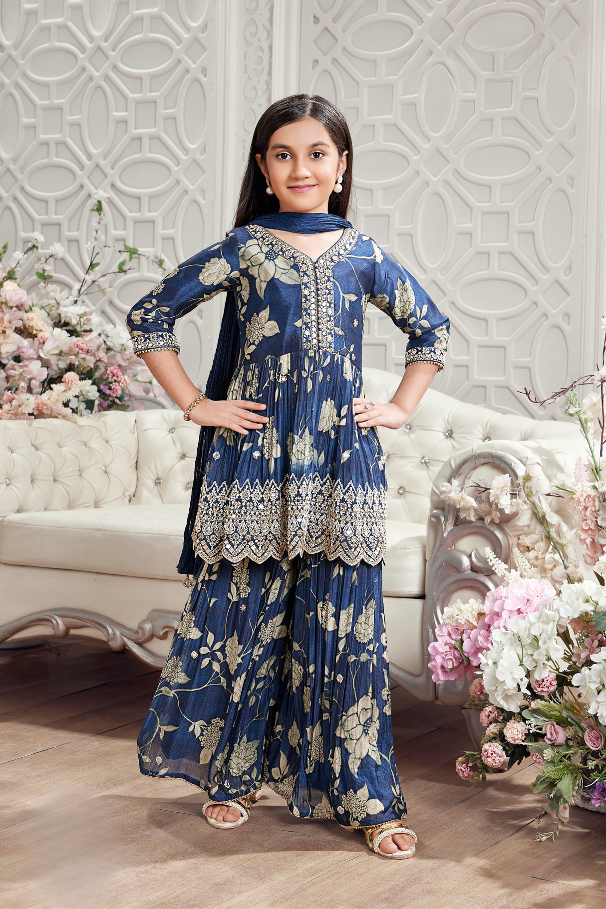 Young girl wearing an elegant navy blue gharara suit with a cream and gold floral print, a heavily embroidered V-neck kurti, and flowing tiered gharara pants.