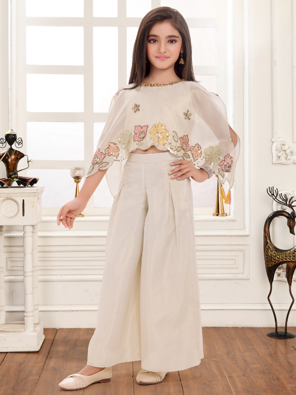 Young girl modeling a cream/off-white ethnic set with a short top, sheer embroidered cape, and pleated wide-leg palazzo pants.