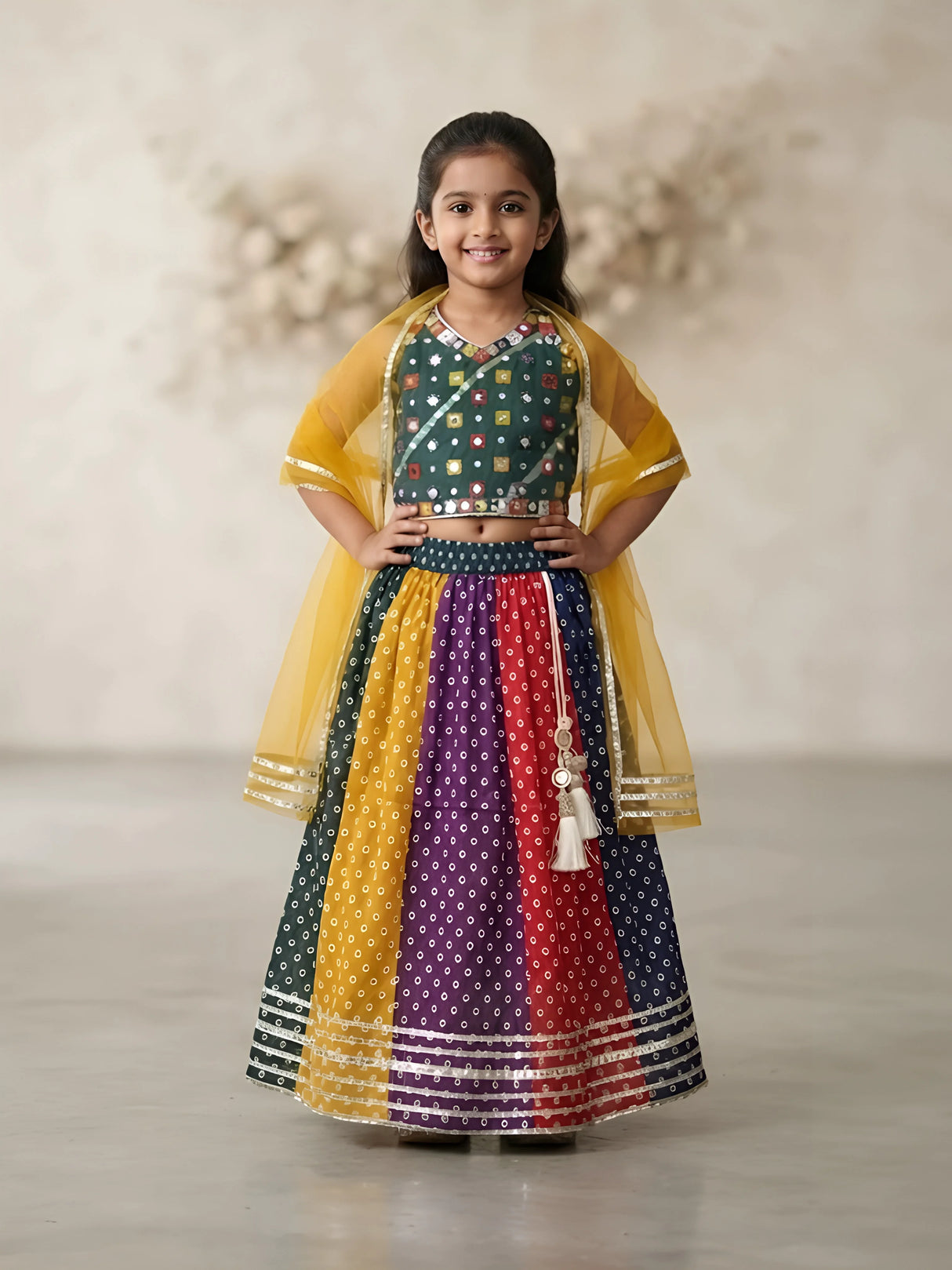 Young girl wearing a green mirror work choli blouse paired with a multi-colored Bandhani print lehenga skirt and yellow dupatta.