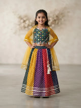 Young girl wearing a green mirror work choli blouse paired with a multi-colored Bandhani print lehenga skirt and yellow dupatta.