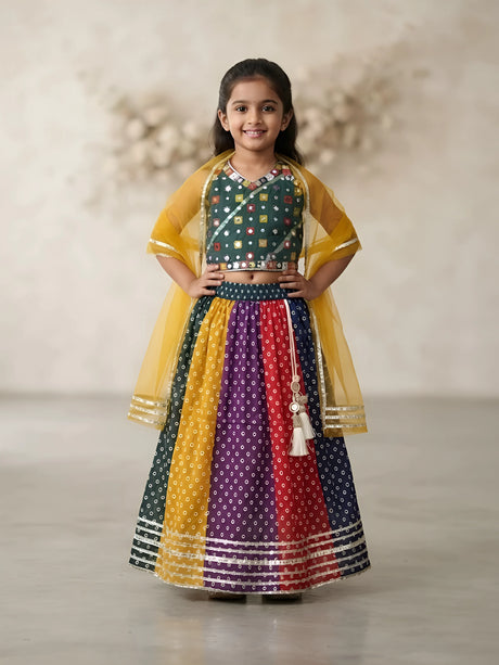 Young girl wearing a green mirror work choli blouse paired with a multi-colored Bandhani print lehenga skirt and yellow dupatta.