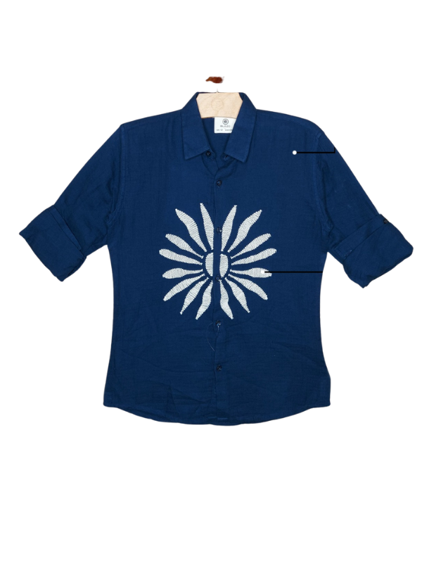 Boys' navy blue long-sleeve shirt with sleeves rolled up, featuring a large, central white abstract starburst or floral design. The shirt is displayed on a wooden hanger.