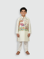 A young boy standing and smiling, wearing a cream/off-white long-sleeved kurta and pajama set with beautiful, detailed multi-color bird and floral embroidery across the chest.