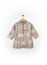 Boys' pink and multicolor geometric printed kurta with embellished neckline and three-quarter sleeves, paired with a cream pajama, hanging on separate hangers.