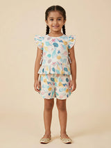A young girl wearing a matching mint green and off-white shorts set featuring a colorful sea shell print, a peplum top with flutter sleeves, and side ties.