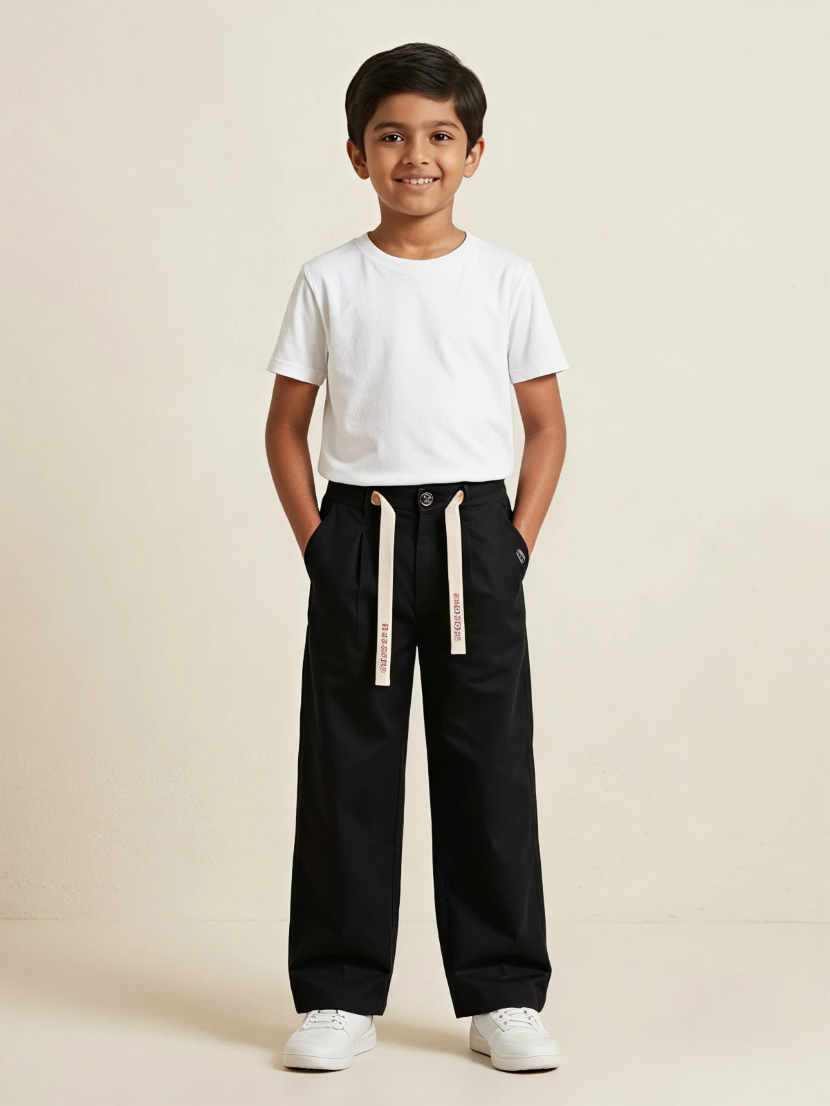 Young boy wearing black casual loose-fit trousers with off-white printed drawstrings and a plain white t-shirt.