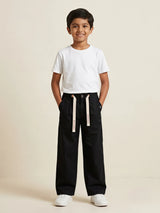 Young boy wearing black casual loose-fit trousers with off-white printed drawstrings and a plain white t-shirt.
