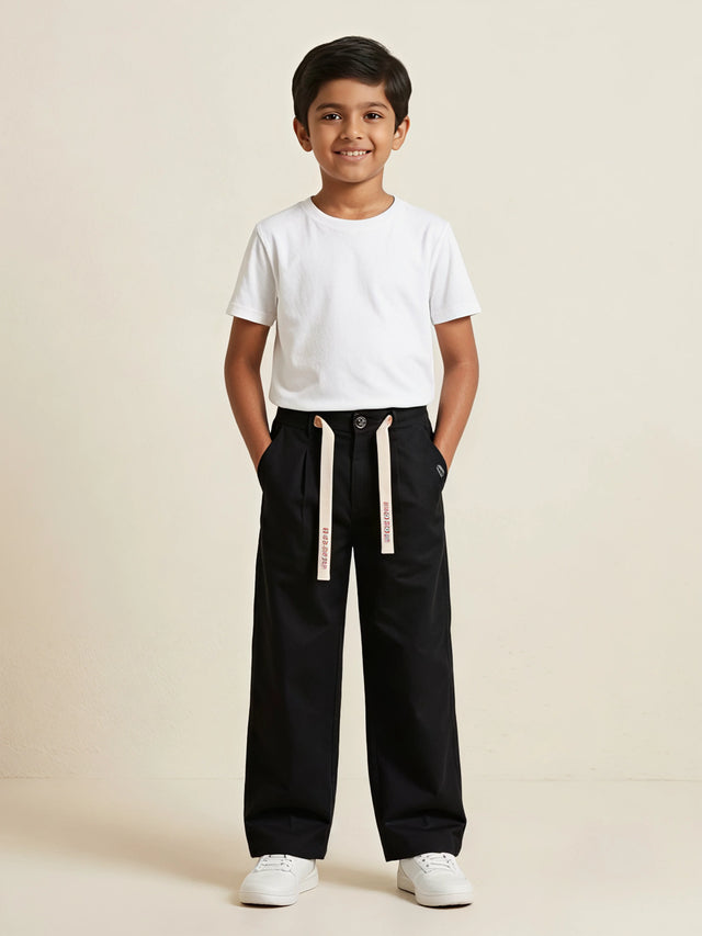 Young boy wearing black casual loose-fit trousers with off-white printed drawstrings and a plain white t-shirt.