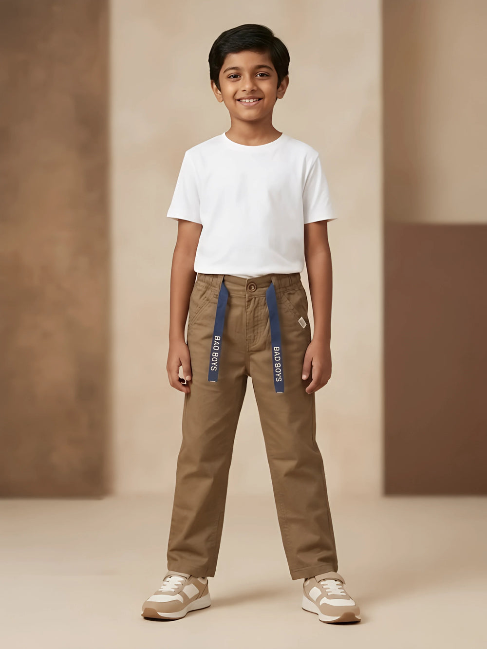 Young boy wearing brown casual trousers with navy blue printed tape detail and a white t-shirt.