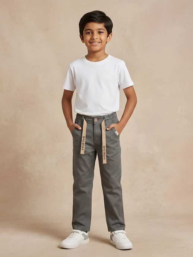Young boy wearing stylish grey casual trousers with drawstring details and white t-shirt