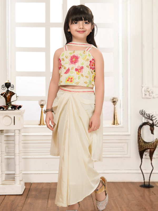 Young girl modeling a cream/off-white ethnic set with a sleeveless floral embroidered crop top and draped dhoti-style pants.