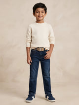 Young boy wearing dark blue regular fit jeans paired with a cream sweater and casual sneakers