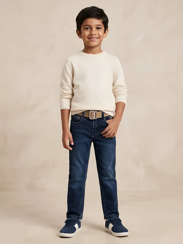 Young boy wearing dark blue regular fit jeans paired with a cream sweater and casual sneakers