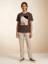 Girl wearing a dark brown round neck short sleeve t-shirt with abstract graphic print and text ILLUMINATE