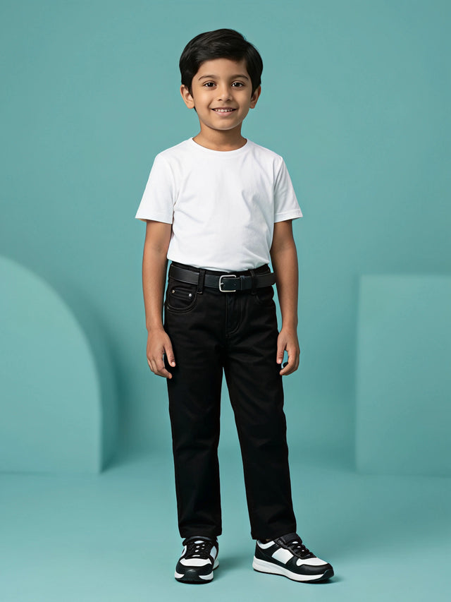 Young boy wearing classic black regular fit jeans styled with a white t-shirt and black sneakers against a light blue background.