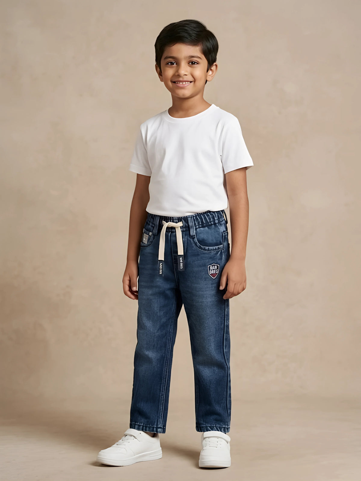 Young boy wearing dark blue elastic waist denim jeans with drawstring detail and white sneakers