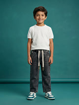Young boy wearing grey washed loose fit drawstring jeans with a white t-shirt and sneakers