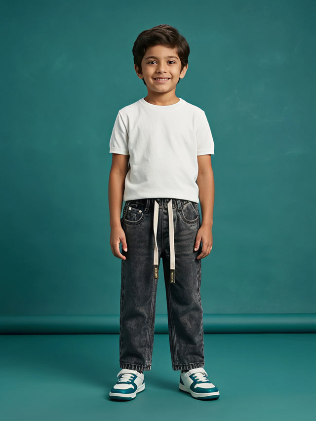 Young boy wearing grey washed loose fit drawstring jeans with a white t-shirt and sneakers