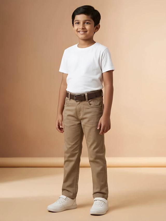 Young boy wearing stylish brown casual pants paired with a white t-shirt and white sneakers