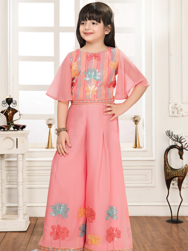 Young girl wearing a peach-colored two-piece set. The crop top has butterfly/bell sleeves and striped, sequined embroidery, paired with wide-leg palazzo pants featuring large floral embroidery near the hem.