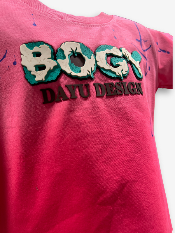 Vibrant fuchsia pink boys' short-sleeve T-shirt with a central "BOGY" graphic with teal and white pattern and scattered blue paint splatters