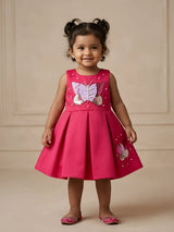Little girl wearing a bright pink sleeveless party frock featuring a sparkling sequined butterfly applique, pearl details, and a box-pleated flared skirt.