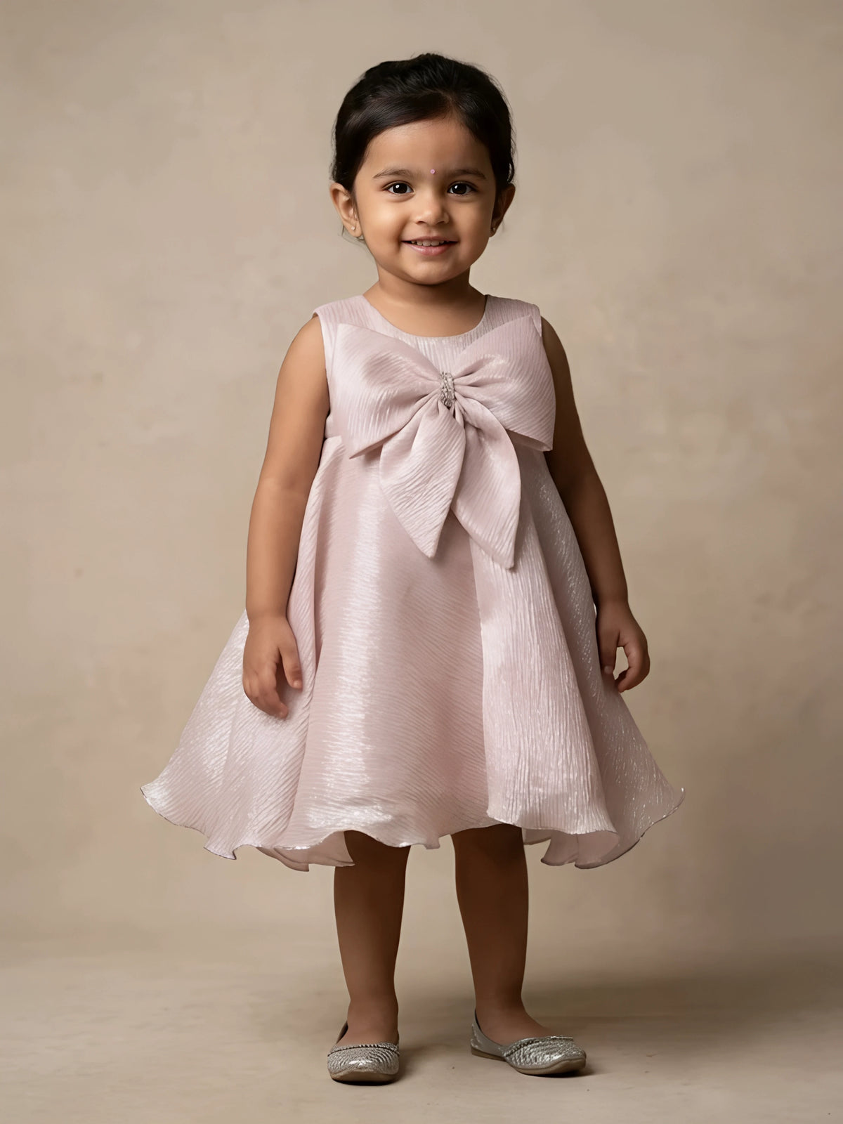 Little girl wearing a stylish cream party wear frock with a large statement bow on top.