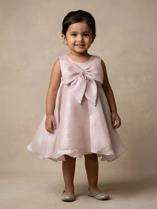 Little girl wearing a stylish cream party wear frock with a large statement bow on top.