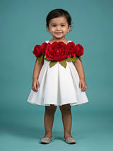 Baby girl wearing a sleeveless white party wear frock decorated with large 3D red roses across the neckline