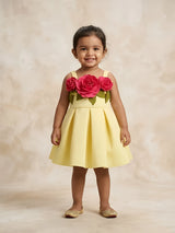 Little girl wearing a bright yellow sleeveless party wear frock with 3D pink rose floral design and box-pleated skirt.