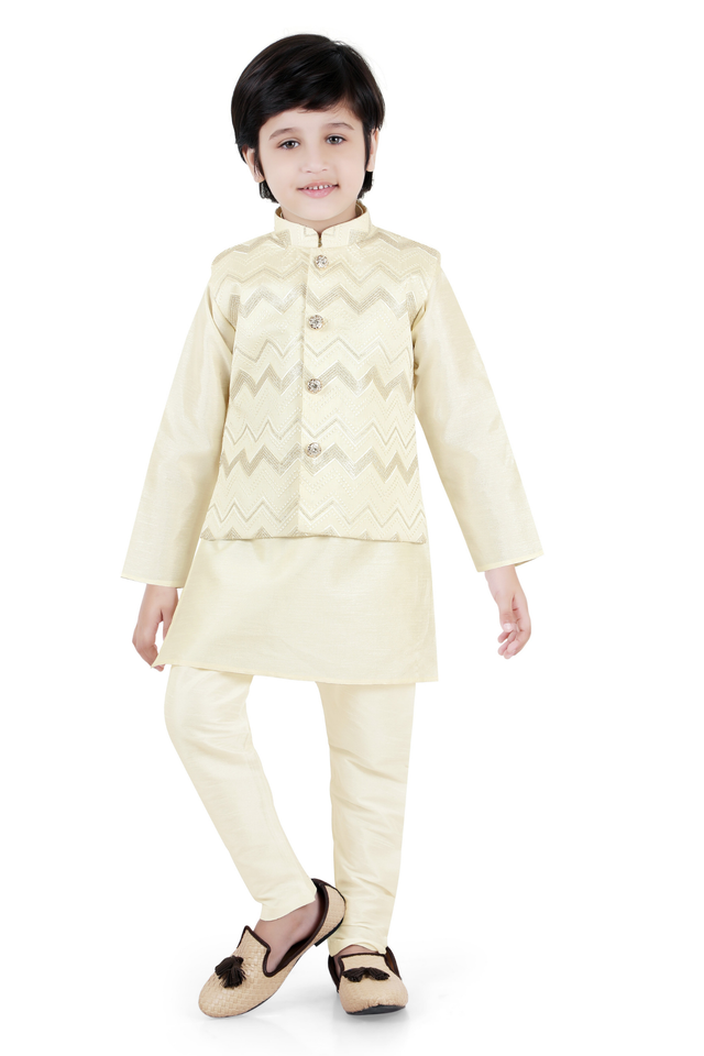  Young boy wearing a long-sleeved cream kurta with white Chikankari-style embroidery, paired with white trousers and cream ethnic shoes.
