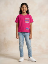 Young girl wearing a bright pink short-sleeve crew neck t-shirt with colourful graphic text print and light blue jeans.