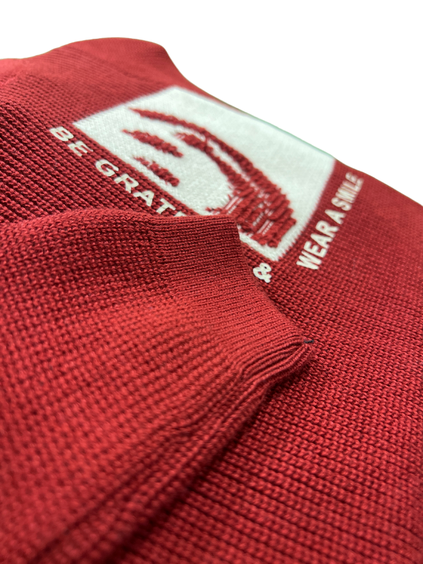 Maroon/Burgundy boys' long-sleeve knit sweater with a ribbed texture, featuring a white contrast panel with a red knitted smiley face and the text "BE GRATEFUL & WEAR A SMILE.