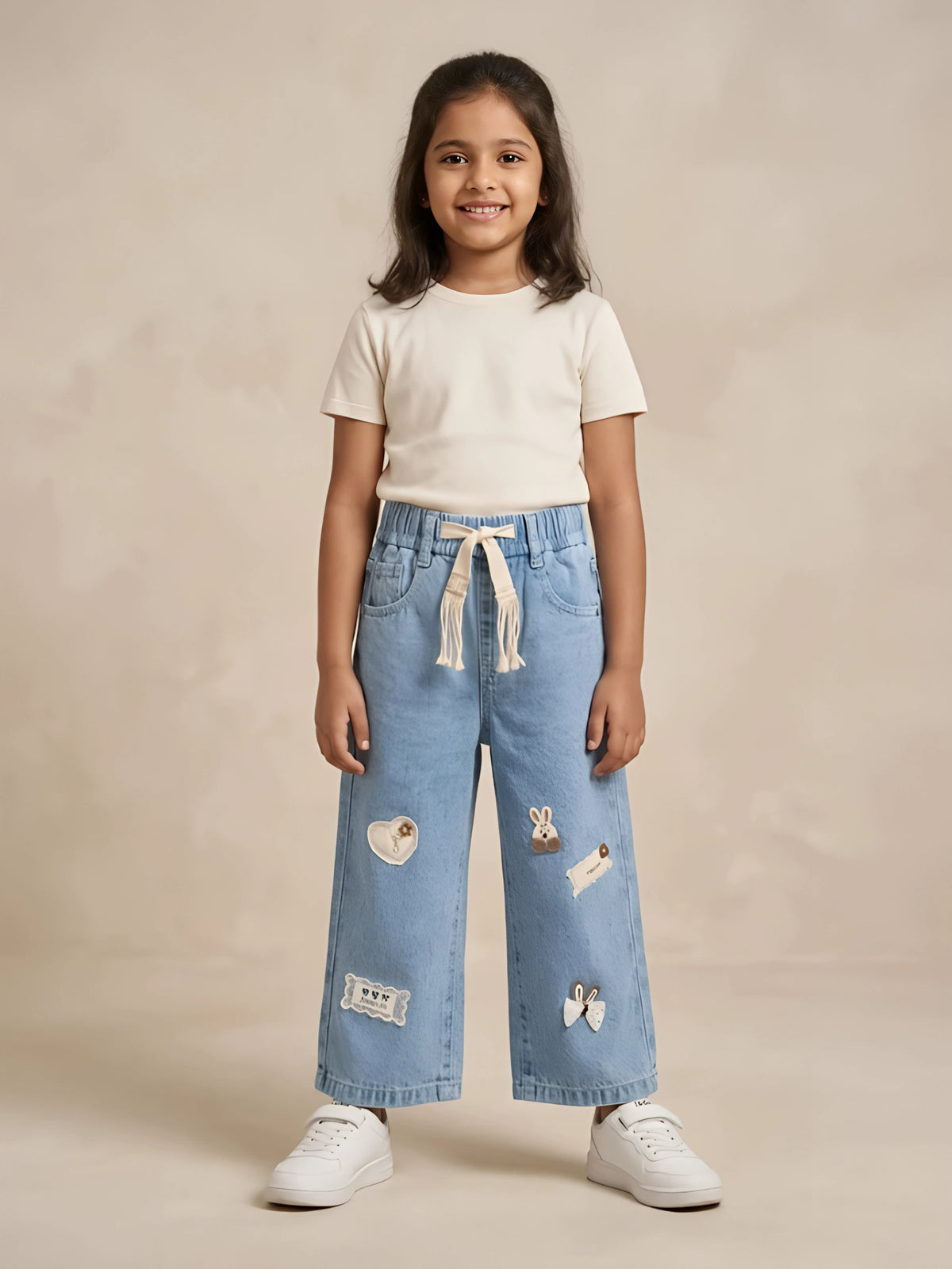 Young girl wearing light blue wide-leg casual pants with decorative patches and a drawstring waistband.
