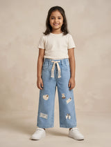 Young girl wearing light blue wide-leg casual pants with decorative patches and a drawstring waistband.