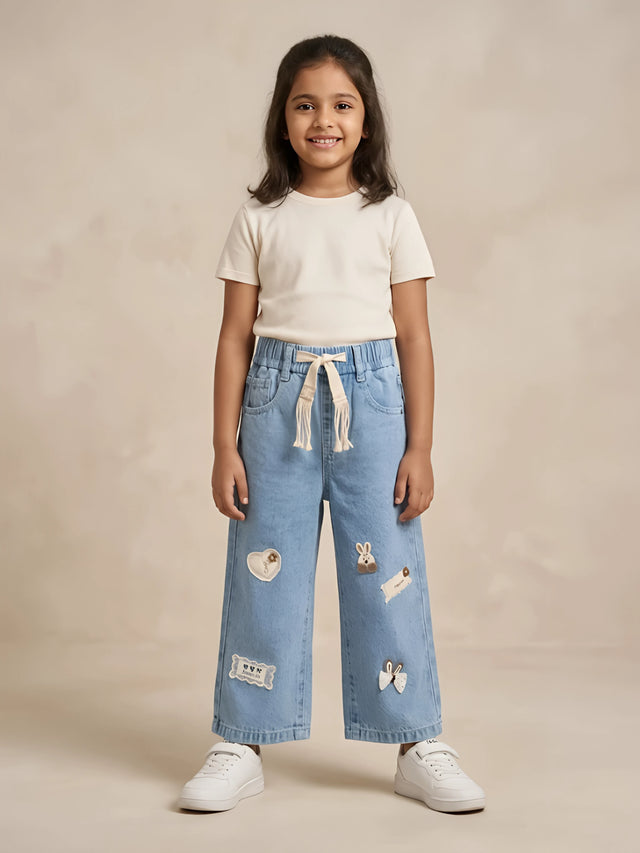 Young girl wearing light blue wide-leg casual pants with decorative patches and a drawstring waistband.