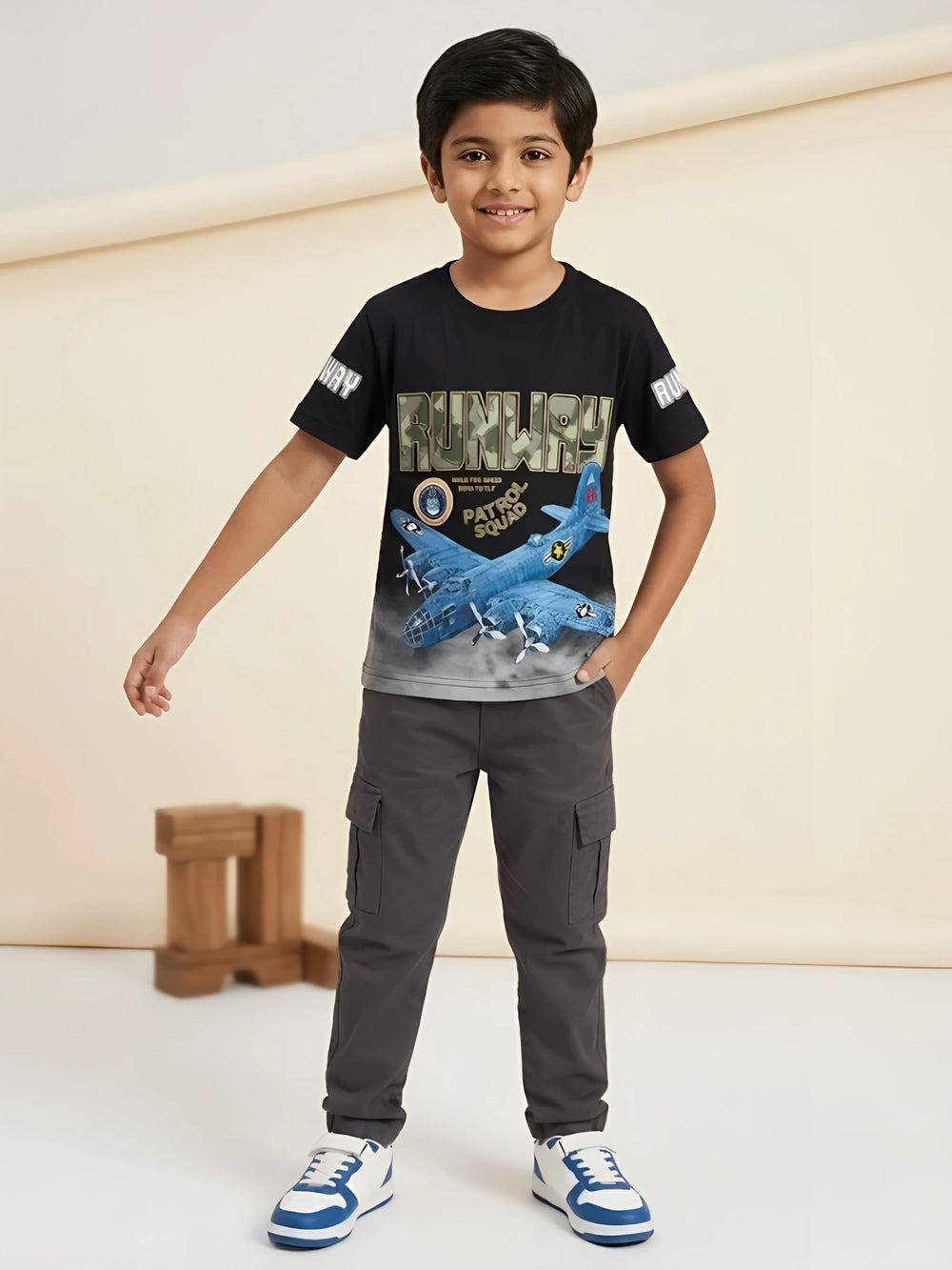 Young boy wearing a black round neck t-shirt featuring a camo RUNWAY text print and blue airplane graphic.