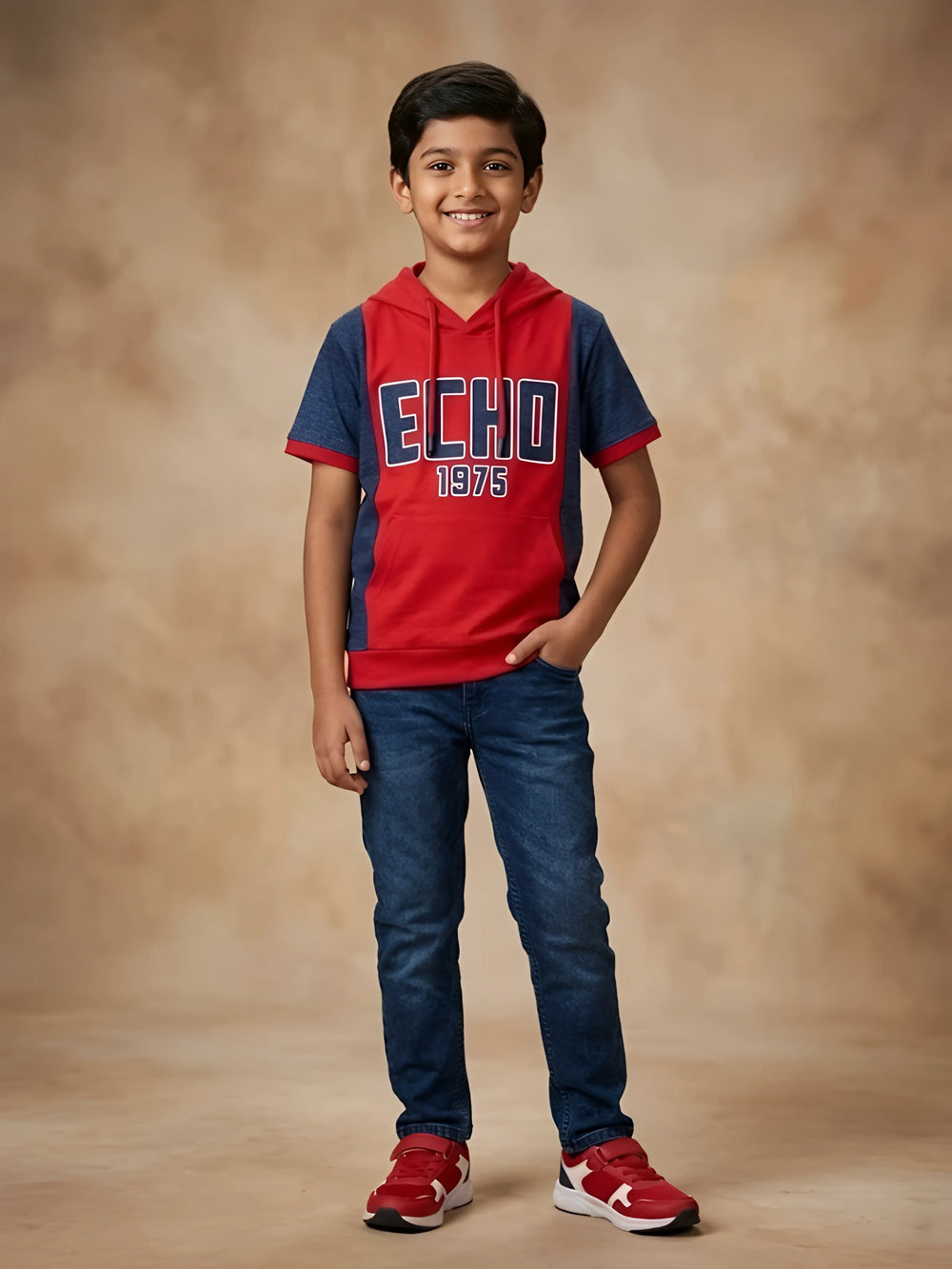 Young boy wearing a red and navy blue hooded short sleeve graphic t-shirt with kangaroo pocket paired with dark blue jeans