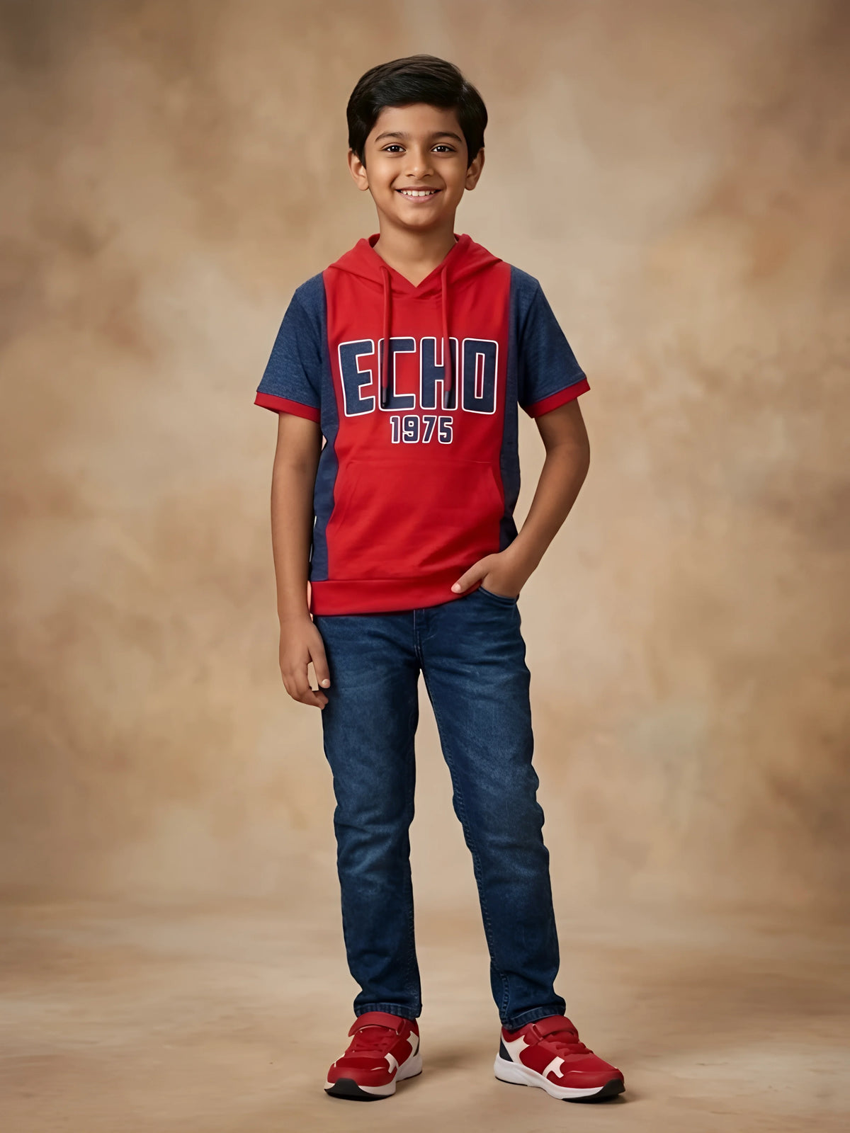 Young boy wearing a red and navy blue hooded short sleeve graphic t-shirt with kangaroo pocket paired with dark blue jeans