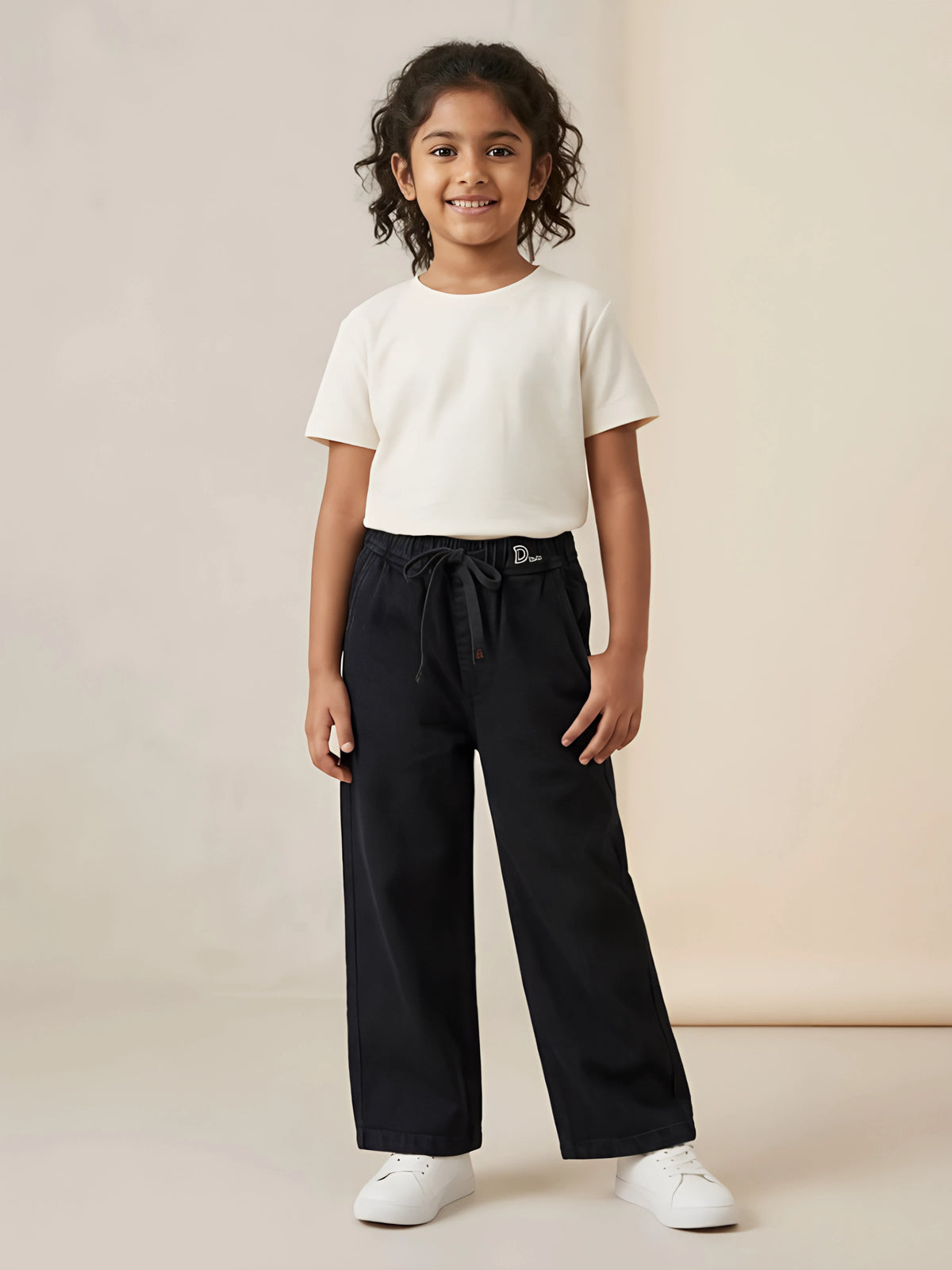 Young girl wearing black wide-leg casual pants with an elastic drawstring waist and side pockets paired with a white t-shirt.