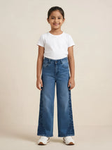 Young girl wearing blue wide-leg casual jeans with dark side-seam floral pattern paired with a white t-shirt and white sneakers