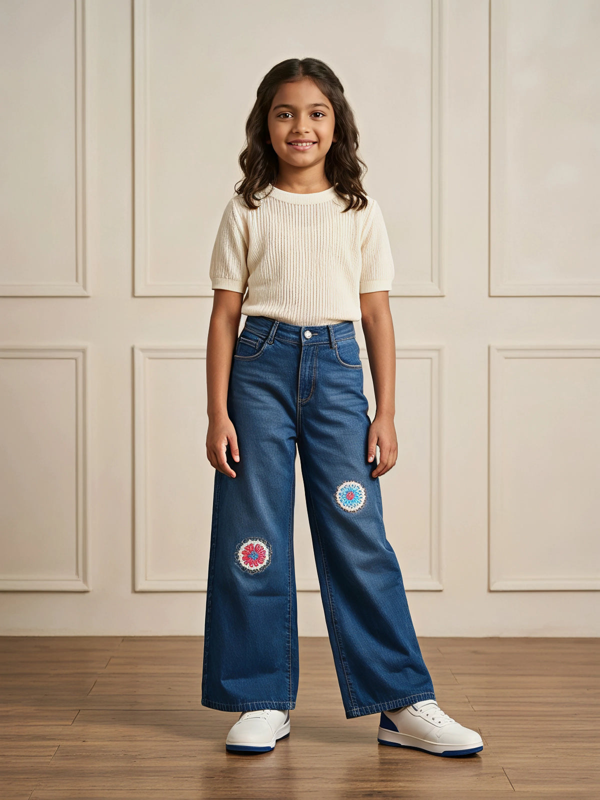 Young girl wearing navy blue wide-leg casual pants with colorful embroidered circular knee patches and a cream top.