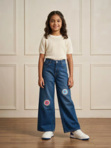 Young girl wearing navy blue wide-leg casual pants with colorful embroidered circular knee patches and a cream top.