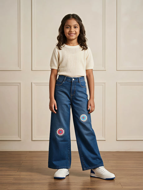 Young girl wearing navy blue wide-leg casual pants with colorful embroidered circular knee patches and a cream top.