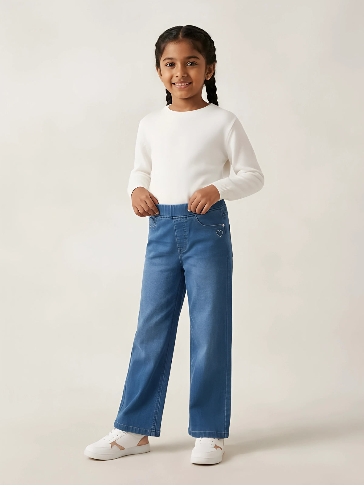 Young girl wearing navy blue straight fit casual pants paired with a white t-shirt and sneakers against a teal background