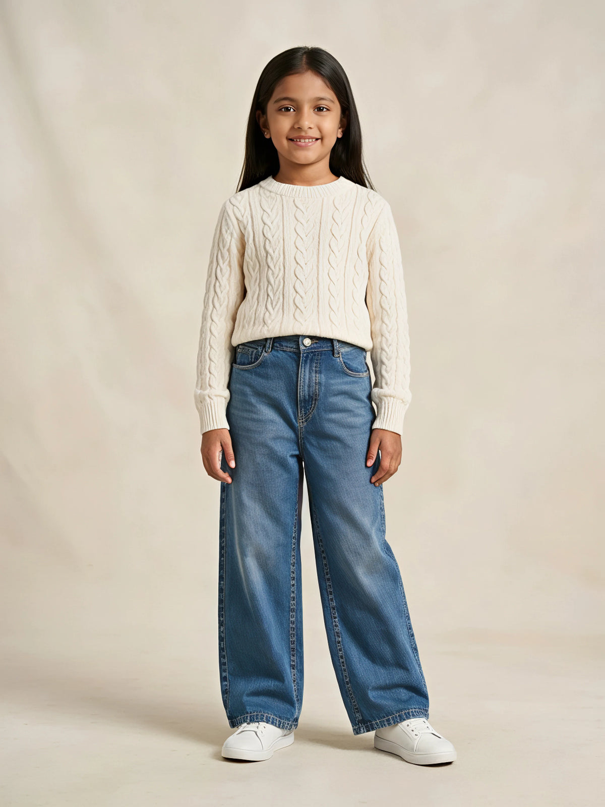 Young girl wearing blue wide leg casual denim pants paired with a cream sweater and white sneakers.