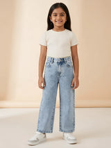 Young girl wearing light blue acid wash wide leg casual pants styled with a white top and sneakers.
