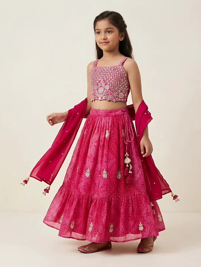 Girls rani pink embroidered choli top with matching bandhani printed flared lehenga skirt and drape with tassels.
