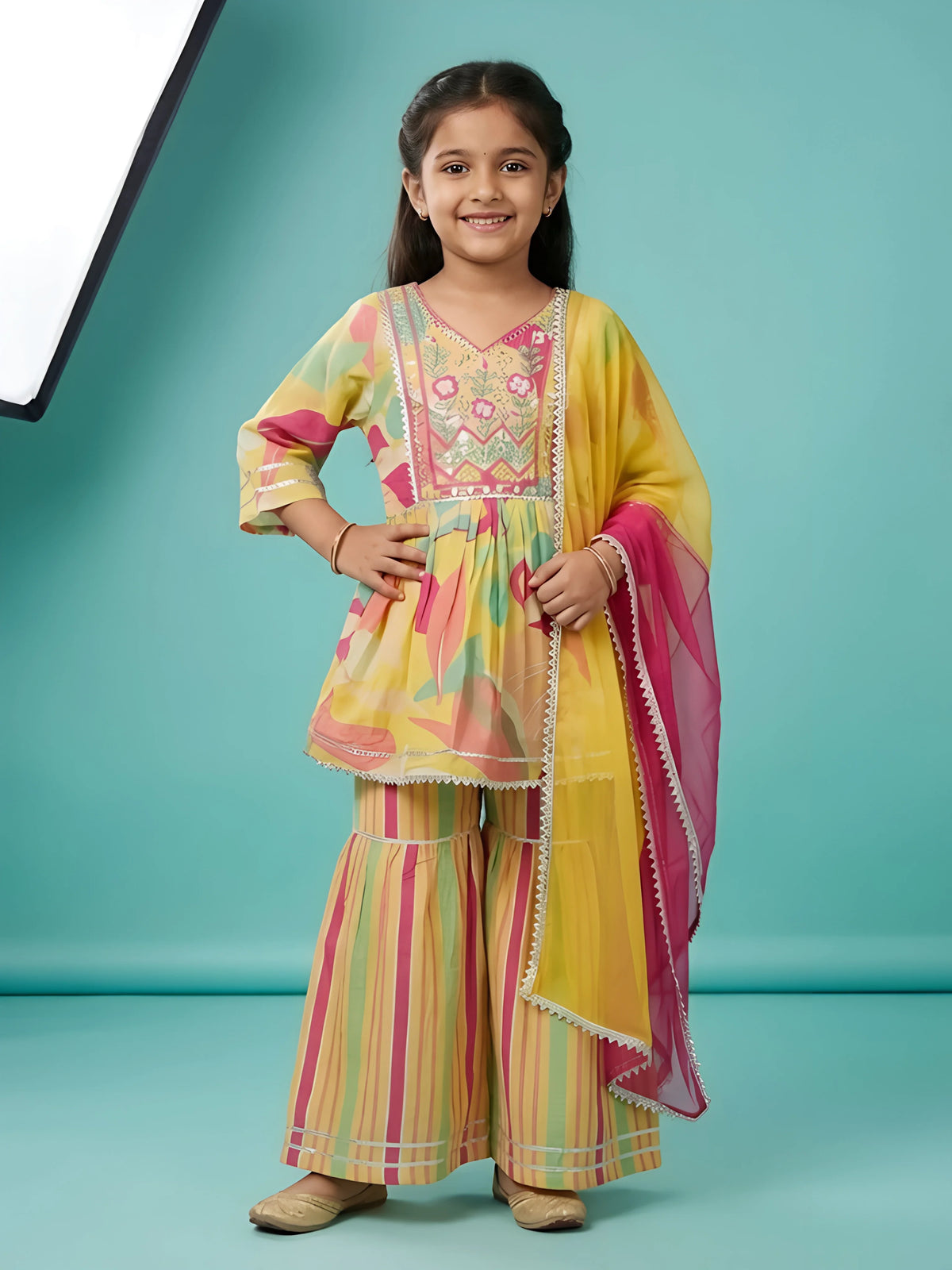 Young girl wearing a bright yellow printed sharara set with pink border dupatta and embroidered kurti neckline