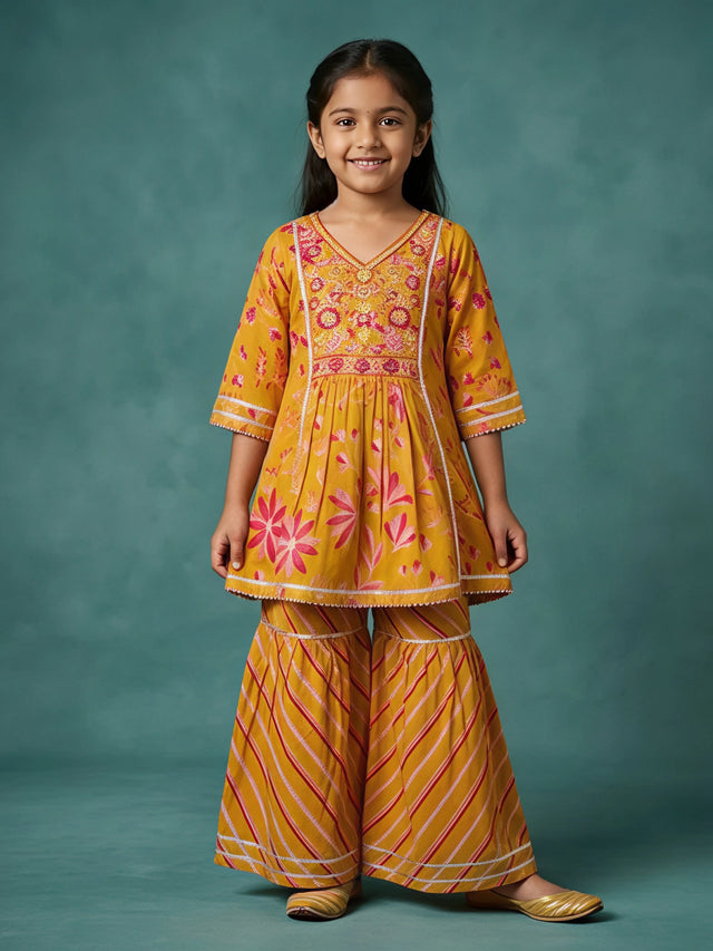 Young girl wearing a mustard yellow floral printed short tunic with embroidered V-neckline paired with matching striped sharara pants.
